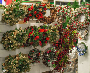Christmas shopping. Many decorated with red elements and cones green christmas wreaths hanging in store for sale.