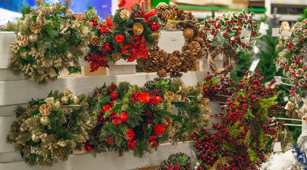 Fototapeta na wymiar Christmas shopping. Many decorated with red elements and cones green christmas wreaths hanging in store for sale.