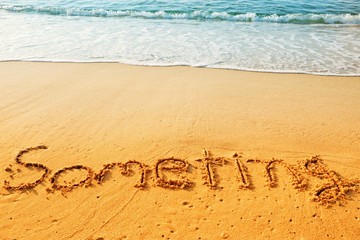 The word someting handwriting on sand beach with blue waves background.