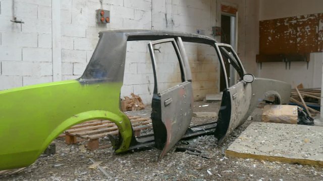 Right sheet metal of a destroyed car. Painted in green and gray, in an abandoned shed with differents objects on the ground.