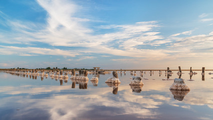 Fototapeta premium sunset on a pink salt lake, a former mine for the extraction of pink salt. row of wooden pegs overgrown with salt.