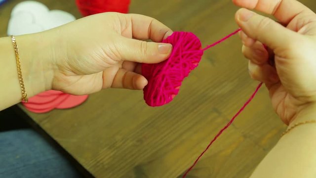 The girl makes a suverner from a red heart of cardboard and thread. Time laps.