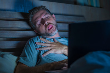 man alone in bed playing cybersex using laptop computer watching porn sex movie late at night with...