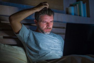 Fototapeta premium attractive and relaxed internet addict man networking concentrated late at night on bed with laptop computer in social media addiction or workaholic businessman concept
