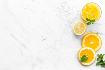 Orange juice and citrus cocktails. Juice in glass near cut orange and lemon, crushed ice, green mint on white stone background top view copy space