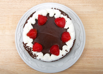 Top view flay lay Chocolate cake frosting in vanilla cream with chocolate glaze topping surrounded by fresh cut strawberries dipped in glaze. Chocolate chip morsels pressed into the side of cake.
