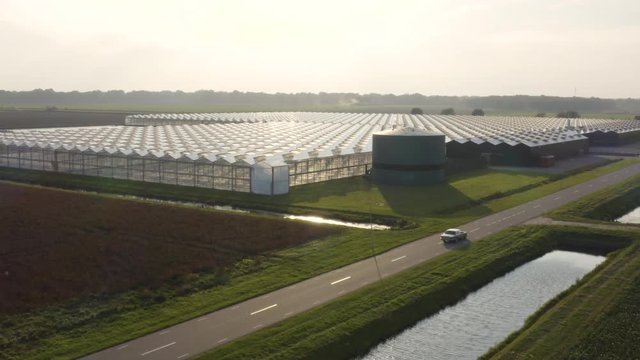 A drone shot of a car passing by greenhouses in the Netherlands