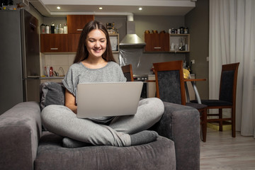 young woman communicates in social networks with laptop, girl sitting at home in chair with laptop