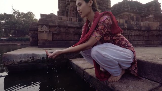 Young Indian woman raises sacred water in offering, slow motion with temple in background. 2x slow motion