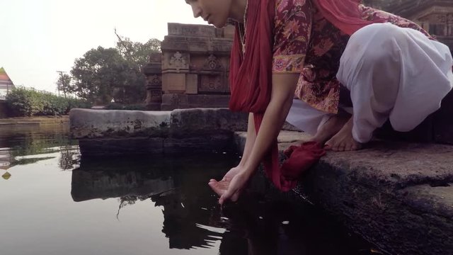 Young Indian woman raises sacred water in offering, slow motion, temple in background. 2x slow motion