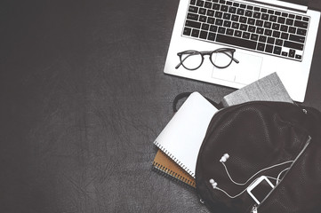 Laptop, backpack, books, notebook, headphones and glasses on black background. Top view
