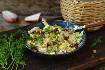Herring salad with peas and mayonnaise in a blue bowl on a wooden background