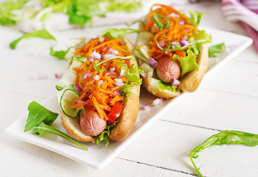 Hot dog with  cucumber, carrot, tomato and lettuce on wooden background. Fast food menu.