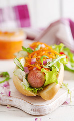 Hot dog with  cucumber, carrot, tomato and lettuce on wooden background. Fast food menu.