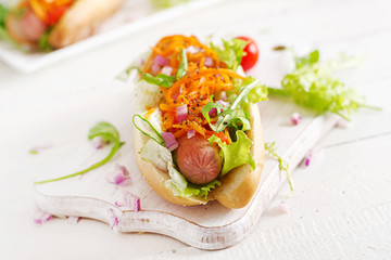 Hot dog with  cucumber, carrot, tomato and lettuce on wooden background. Fast food menu.