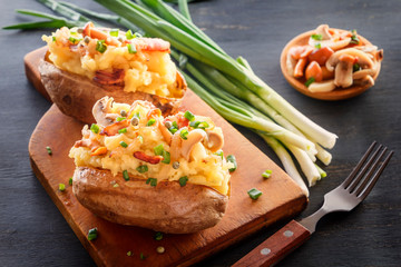 Baked potatoes with bacon, mushrooms and green onions in a rustic style on a wooden board. Close-up