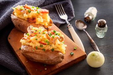 Baked potatoes with bacon and mushrooms in a rustic way on a wooden board. Close-up.