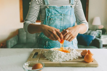 A woman cracking an egg and preparing fresh pasta from scratch at home. 