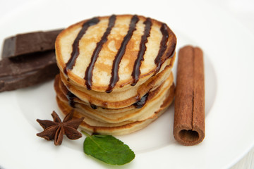 Pancakes on a white plate decorated with fresh mint, cinnamon and chocolate
