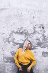 Blond girl in a yellow sweater and in a black skirt against a gray wall background