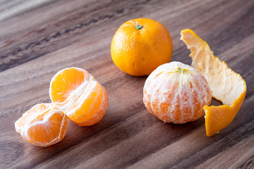 Three satsuma oranges on a rustic wood table, two oranges peeled, one sectioned, and peels on the...