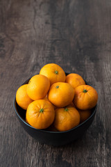 Black bowl of satsuma oranges on a rustic wood table