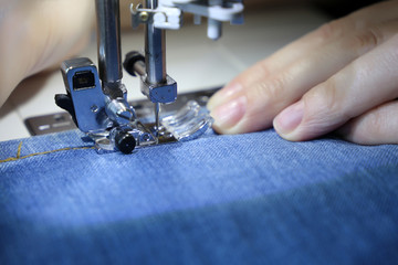 Woman working on the sewing machine, female hands close-up. Seamstress sews jeans, concept of mending clothes, textile industry