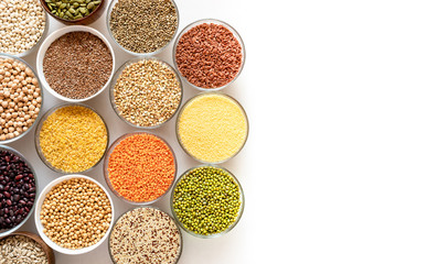 Top view to glass bowls with cereals, beans and seeds on top of white background with copy space on the right.