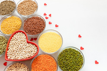 Top view to glass bowls with superfood with red heart-shaped bowl on white background.