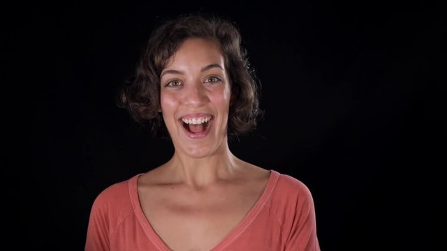 Surprised and excited, a young woman, isolated against a black studio background, looks at the camera and expresses her joy