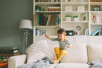 A little boy jumping on the couch at home. 
