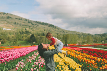 A mother lifting her son into the air in the middle of a tulip field. 