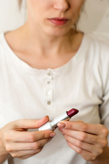 bottle of silver color with bright lipstick for lips, in women's hands on a light background