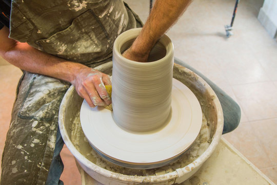     Artist potter in the workshop creating a jug out of earthenware, hands closeup. Twisted potter's wheel. Small aristic craftsmen business concept. 