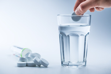 Magnesium pills and cup of clear water on blue white background