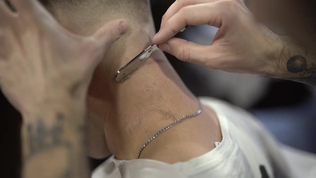 Hands in black gloves of a barberman  shaving customer's hair on the nape/backneck using real blade. Close-up concept
