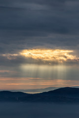 Sunray shines through clouds over the mountains and a sea of fog