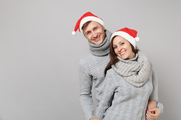 Fototapeta premium Merry fun couple girl guy in red Santa Christmas hat gray sweaters scarves isolated on grey wall background, studio portrait. Happy New Year 2019 celebration holiday party concept. Mock up copy space.