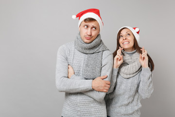 Fototapeta premium Merry fun couple girl guy in red Santa Christmas hat gray sweaters scarves isolated on grey wall background, studio portrait. Happy New Year 2019 celebration holiday party concept. Mock up copy space.