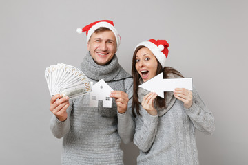 Couple girl guy in red Santa Christmas hat gray sweaters scarves hold money isolated on grey wall background studio portrait. Happy New Year 2019 celebration holiday party concept. Mock up copy space.