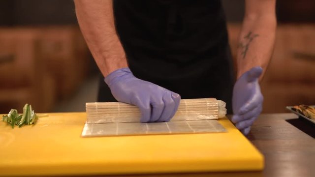 Process of making sushi rolls. Close-up of chef's hands cooking  sushi roll on seaweed mat.
