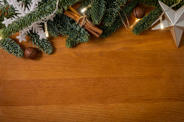 Christmas composition. Christmas tree branches with garland and cinnamon sticks and macadamia sticks on the wooden background