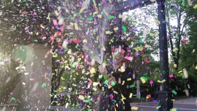 A Recent College Graduate Pops A Bottle Of Champagne While Confetti Rains Around Him In Celebration.