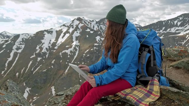 Girl hiker with a tablet sitting on a rock on a background of mountains and lakes, norway