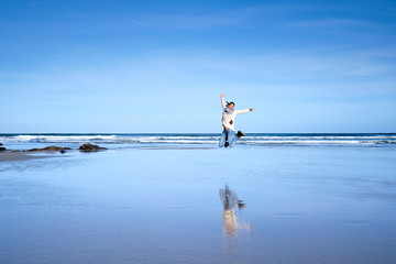 Una chica joven salta de alegría en una playa donde se refleja el cielo durante sus vacaciones