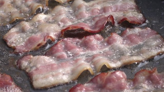 A close up view of bacon sizzling in the frying pan on a stovetop. Cooking  bacon slices for breakfast fry up Stock Photo - Alamy