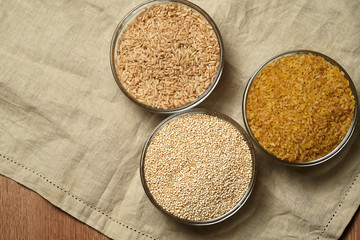Quinoa, bulgur, brown rice in small glass plates against a linen tablecloth. Close up of healthy cereals.