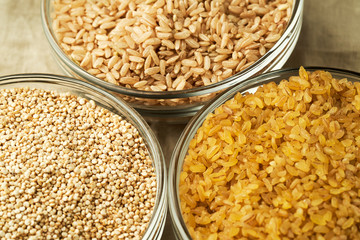 Quinoa, bulgur, brown rice in small glass plates against a linen tablecloth. Close up of healthy cereals.