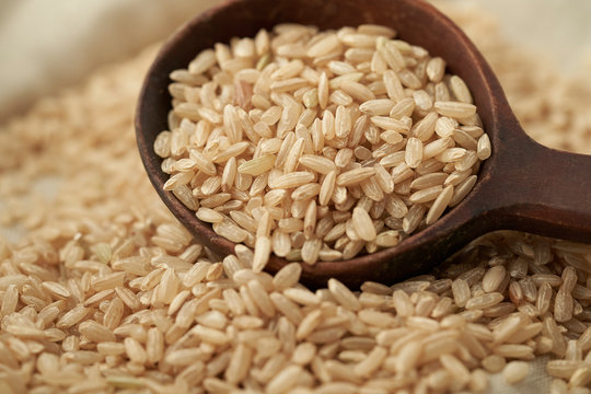 Macro photo of brown rice with a wooden brown spoon on a linen cloth background. Close up of brown rice scooped with a wooden brown spoon.