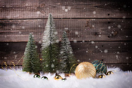 Decorative fir trees,  golden and green balls and fairy lights on white fur background against vintage wooden wall.